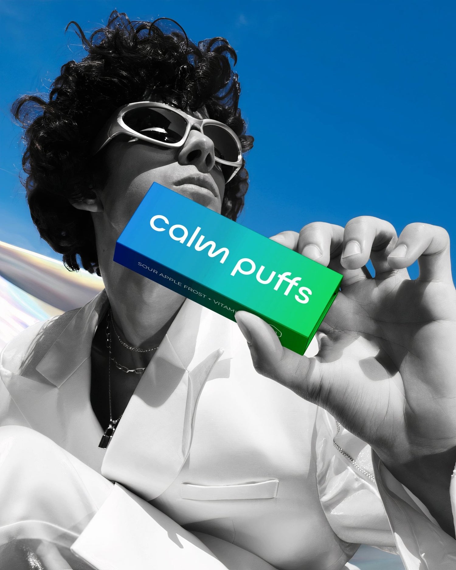 Person holding a Calm Puffs Sour Apple Frost Vitamin C diffuser against a bright blue sky.
