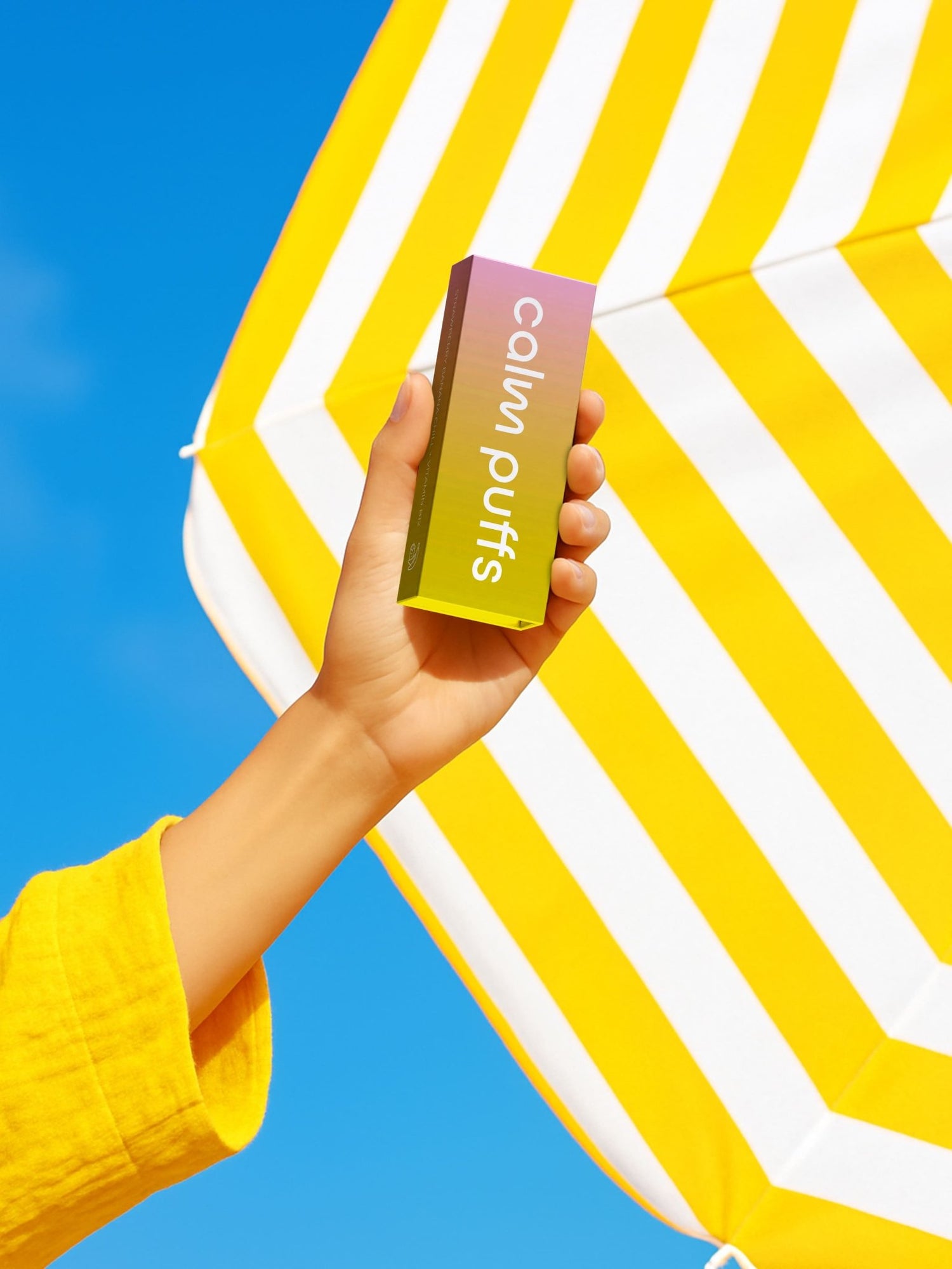 Calm Puffs Strawberry Banana Chill Vitamin B12 diffuser held up against a bright blue sky and yellow striped umbrella