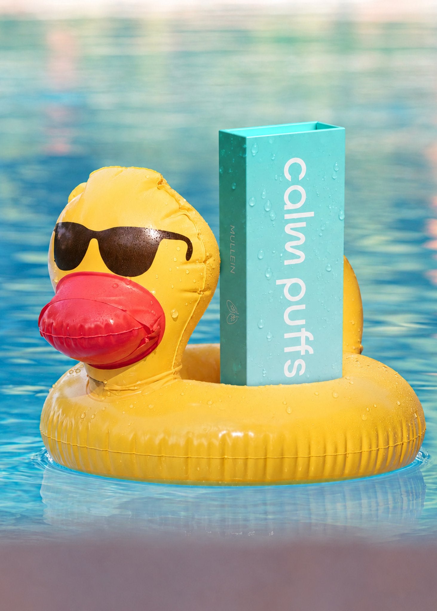 Inflatable yellow duck with sunglasses holding a box labeled 'calm puffs detox diffuser' in a pool.