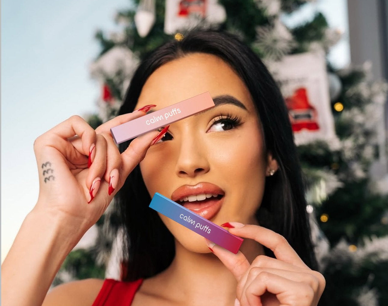 Woman holding two calm puffs in front of a decorated Christmas tree